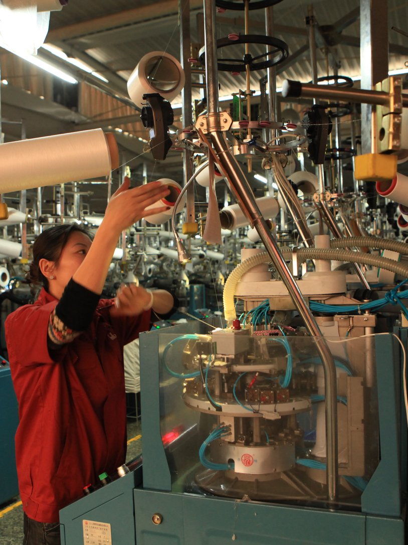 Professional technician operating circular knitting machine at Sichuan Firstlady Knitting Co., Ltd. production facility.